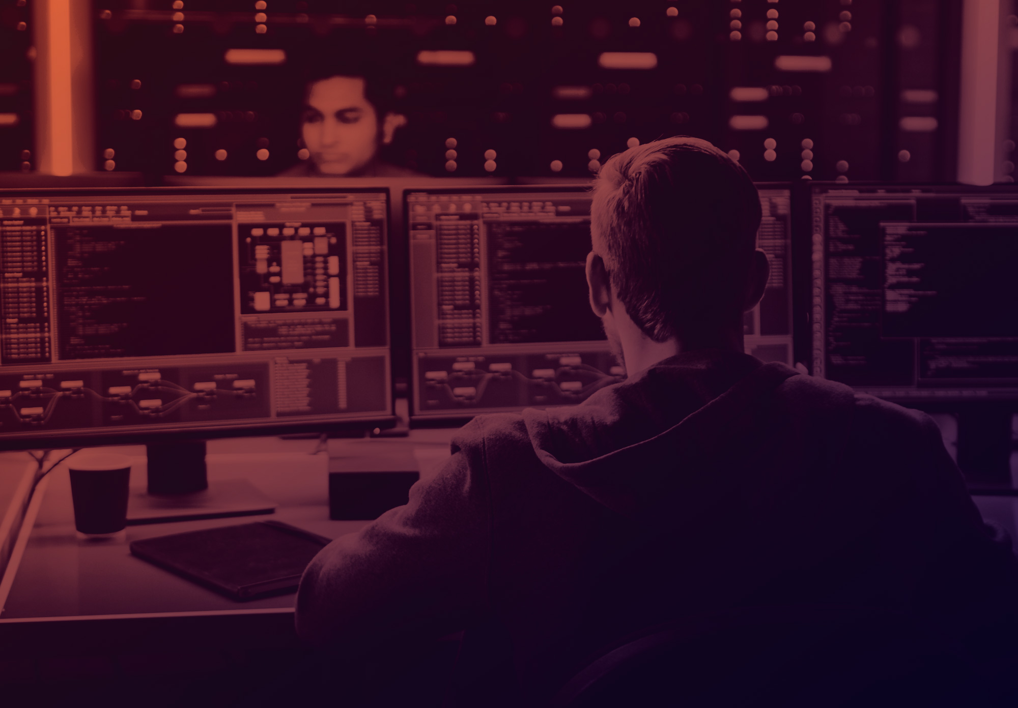 gradiente arancione scuro e viola con un ragazzo di spalle che lavoro su 2 pc