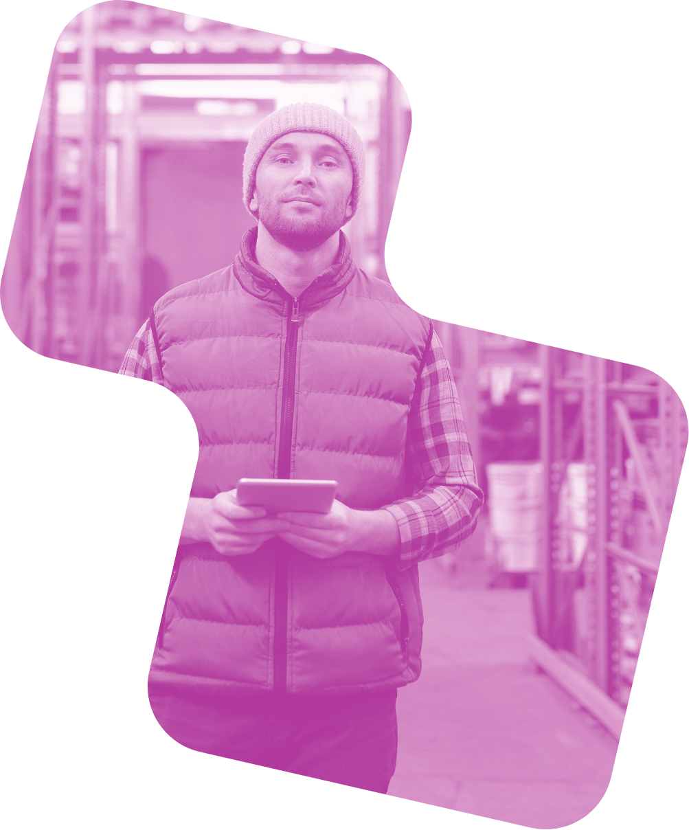 immagine a forma di pixel con gradiente rosa e nello sfondo un ragazzo che cammina dritto con un tablet in mano all'interno di un magazzino