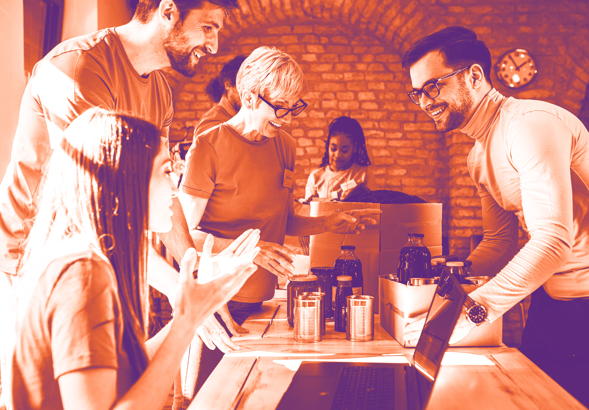 foto con gradiente arancione e viola con ragazzie e ragazze che stanno attorno ad un tavolo e sorridono. sul tavolo c'è un pc, delle scatole, bottiglie e barattoli di latta