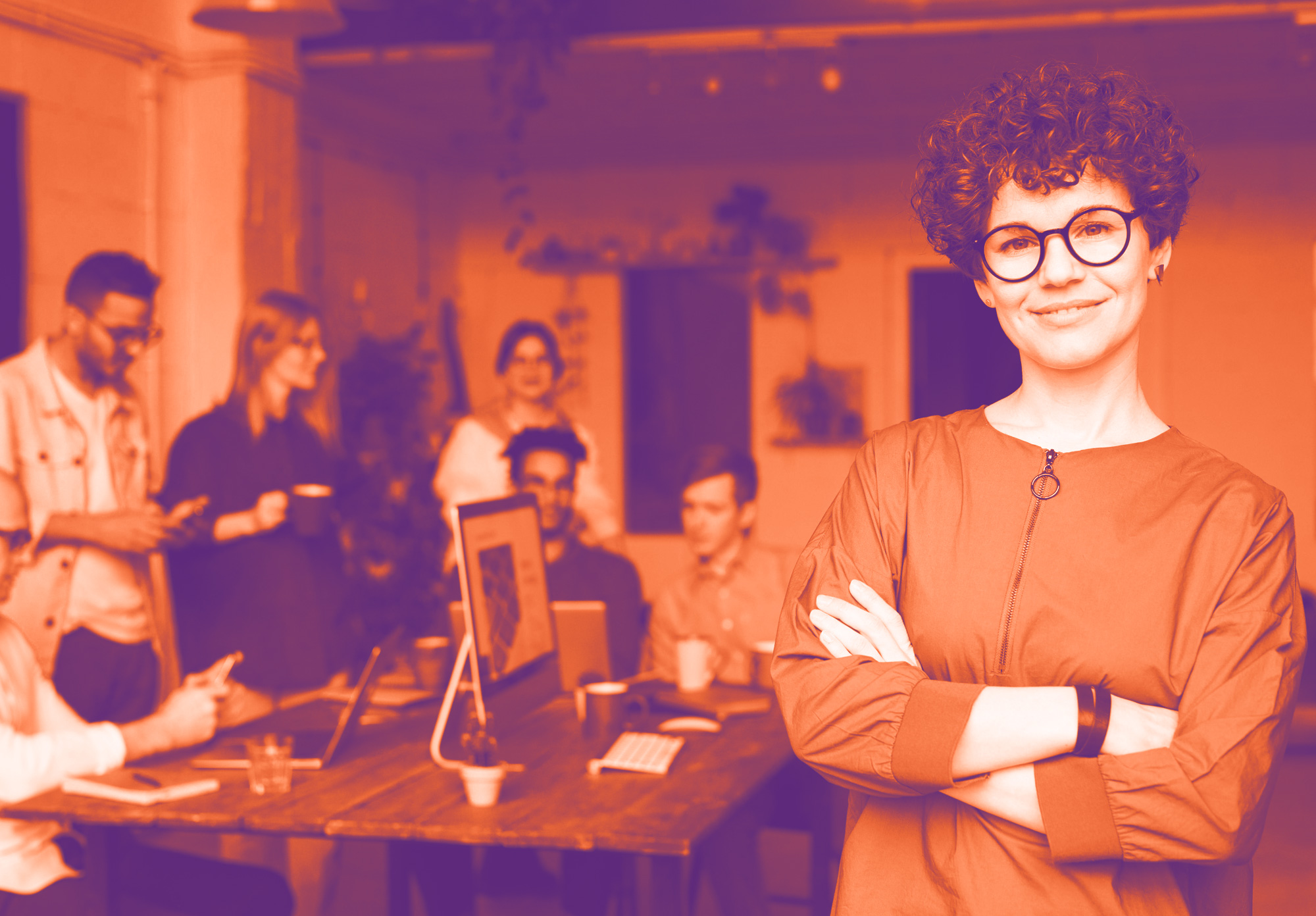 foto con gradiente arancione e viola che ritrae sullo sfondo un gruppo i persone sedute ad un tavolo che parlano. in primo piano una ragazza che guarda dritto con le braccia incrociate