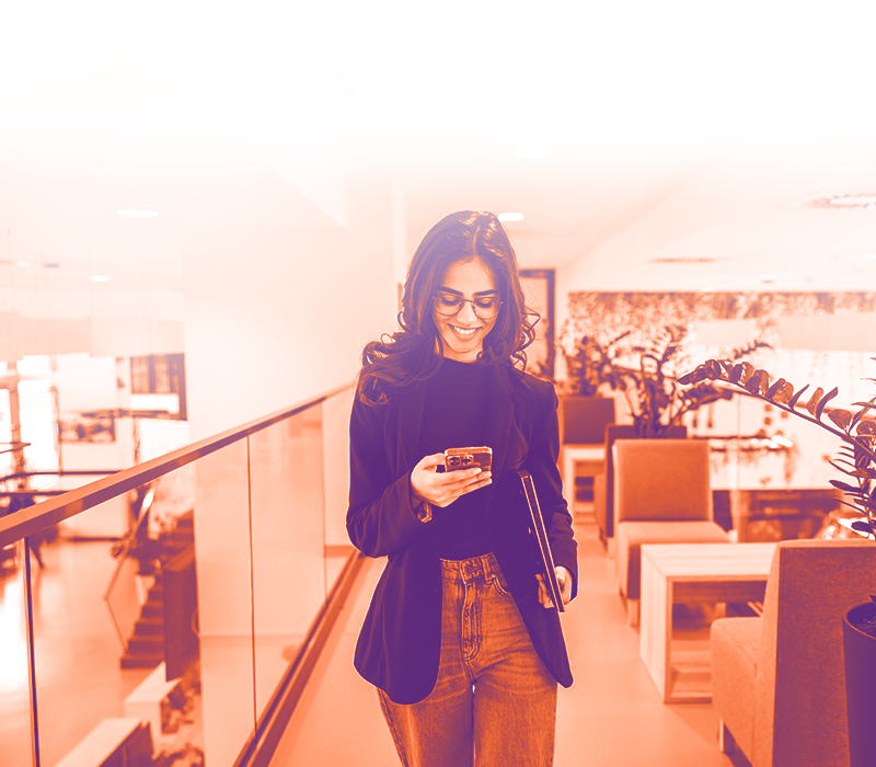 foto con gradiente arancione sfumato sul bianco con una ragazza che cammina su un corridoio guardando il telefono che ha in mano