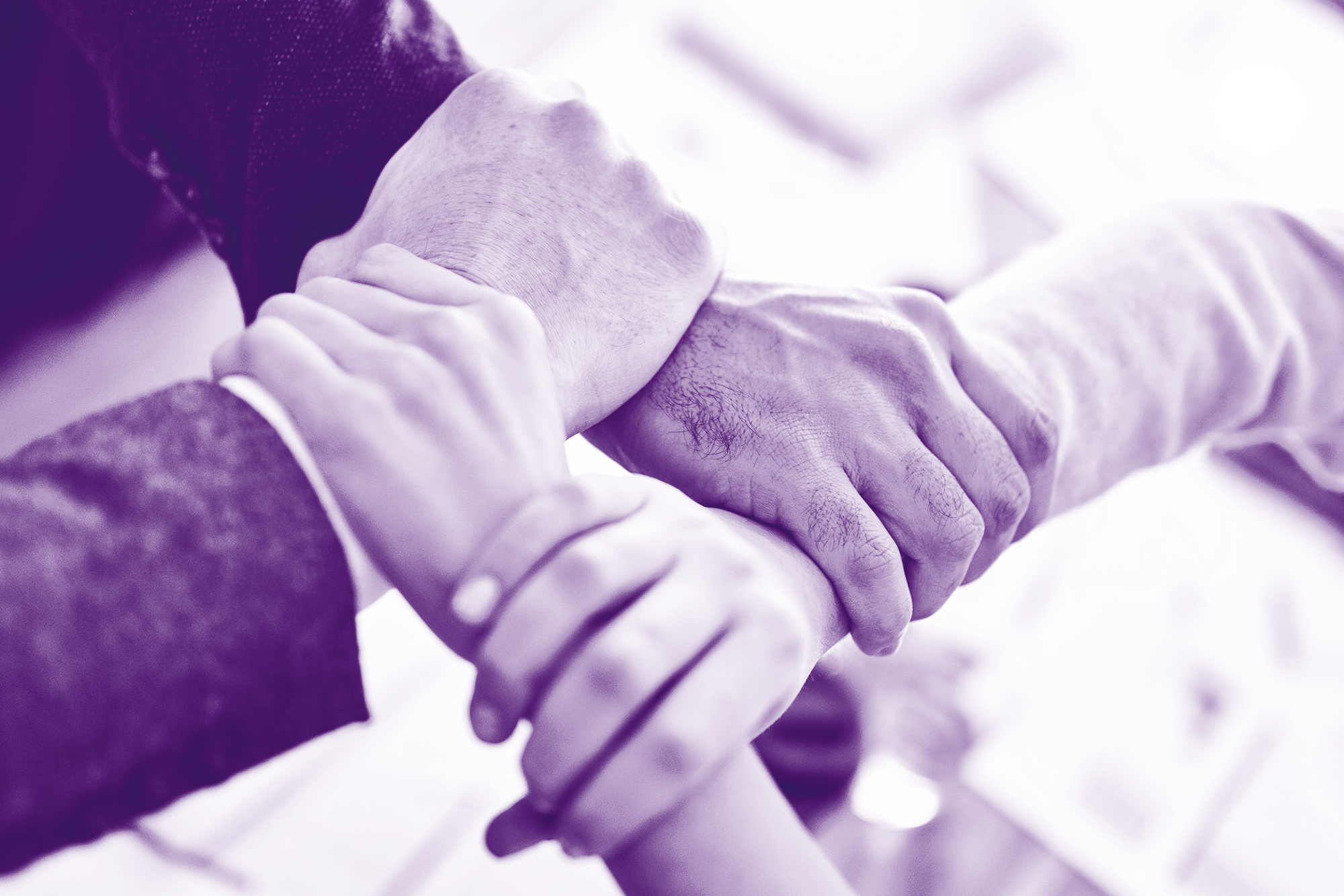 foto con gradiente viola con 4 mani che si stringono il polso che simboleggiano l'unione e la forza