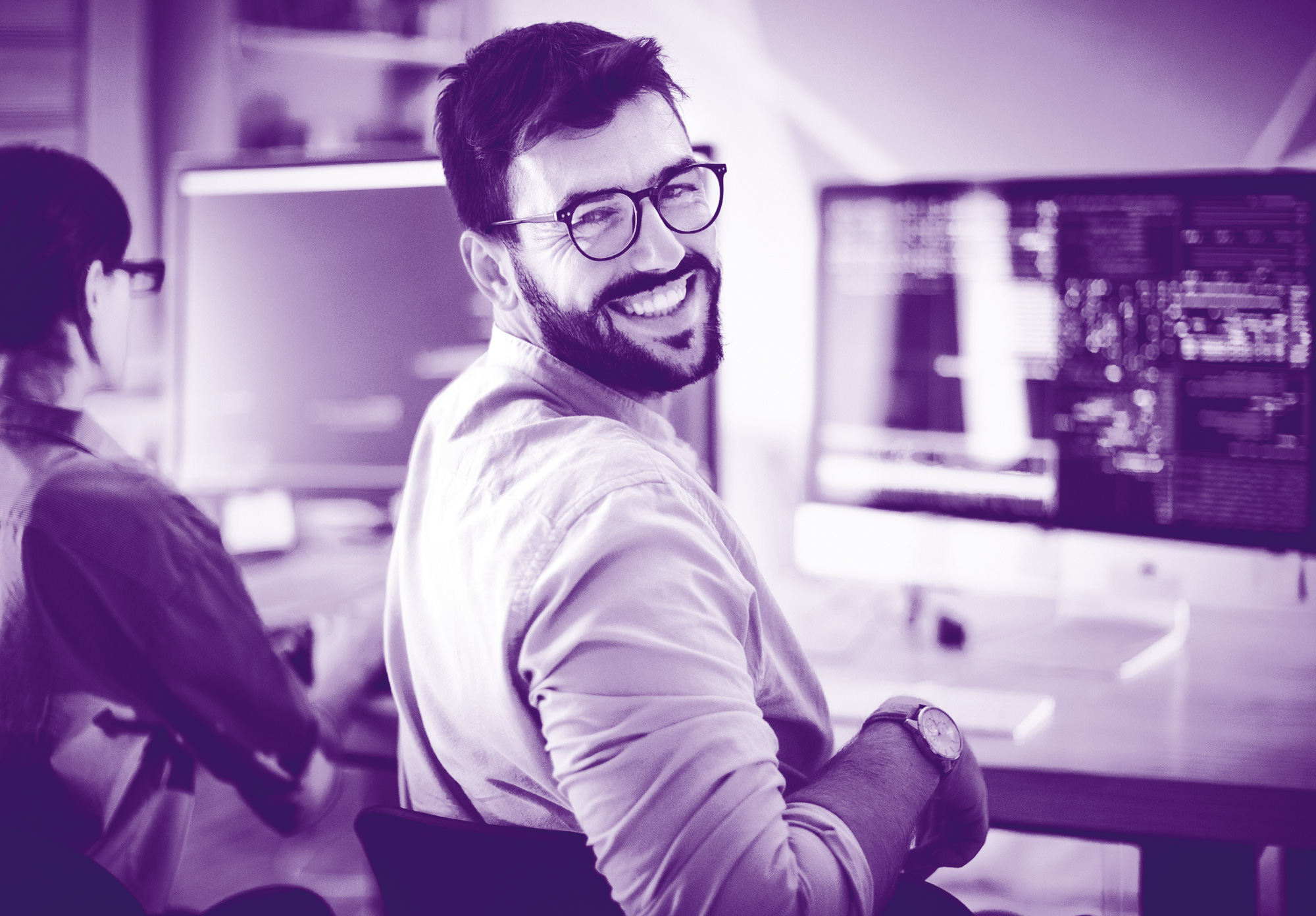 foto di gradiente viola con un uomo seduto al pc che si gira, ci guarda e sorride