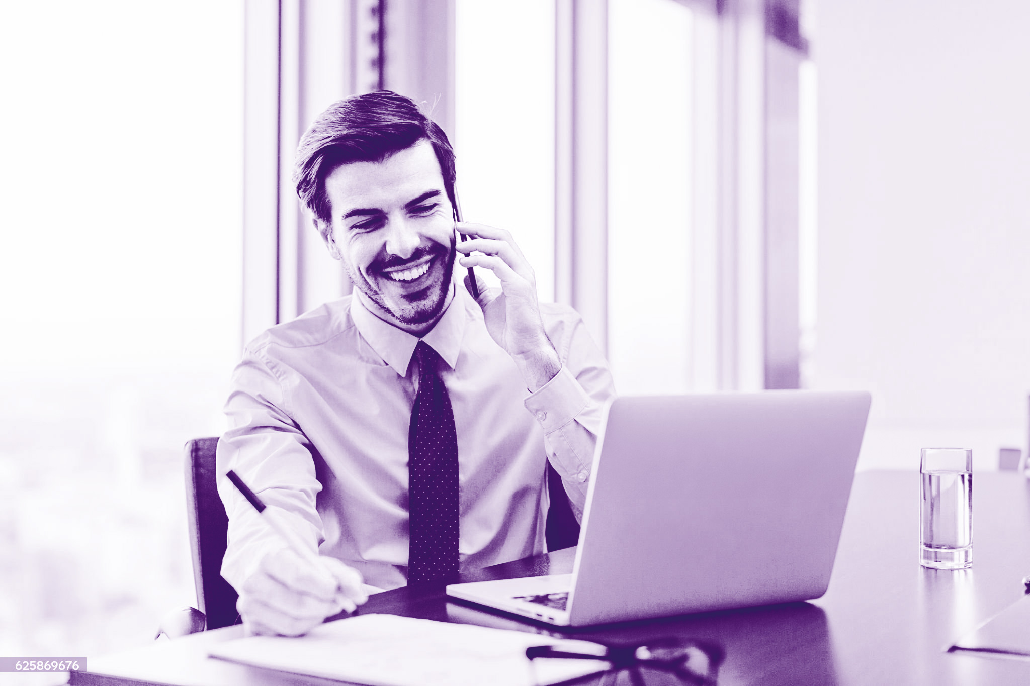 foto con gradiente viola di un uomo seduto alla scrivania al pc, che parla al telefono e prende appunti