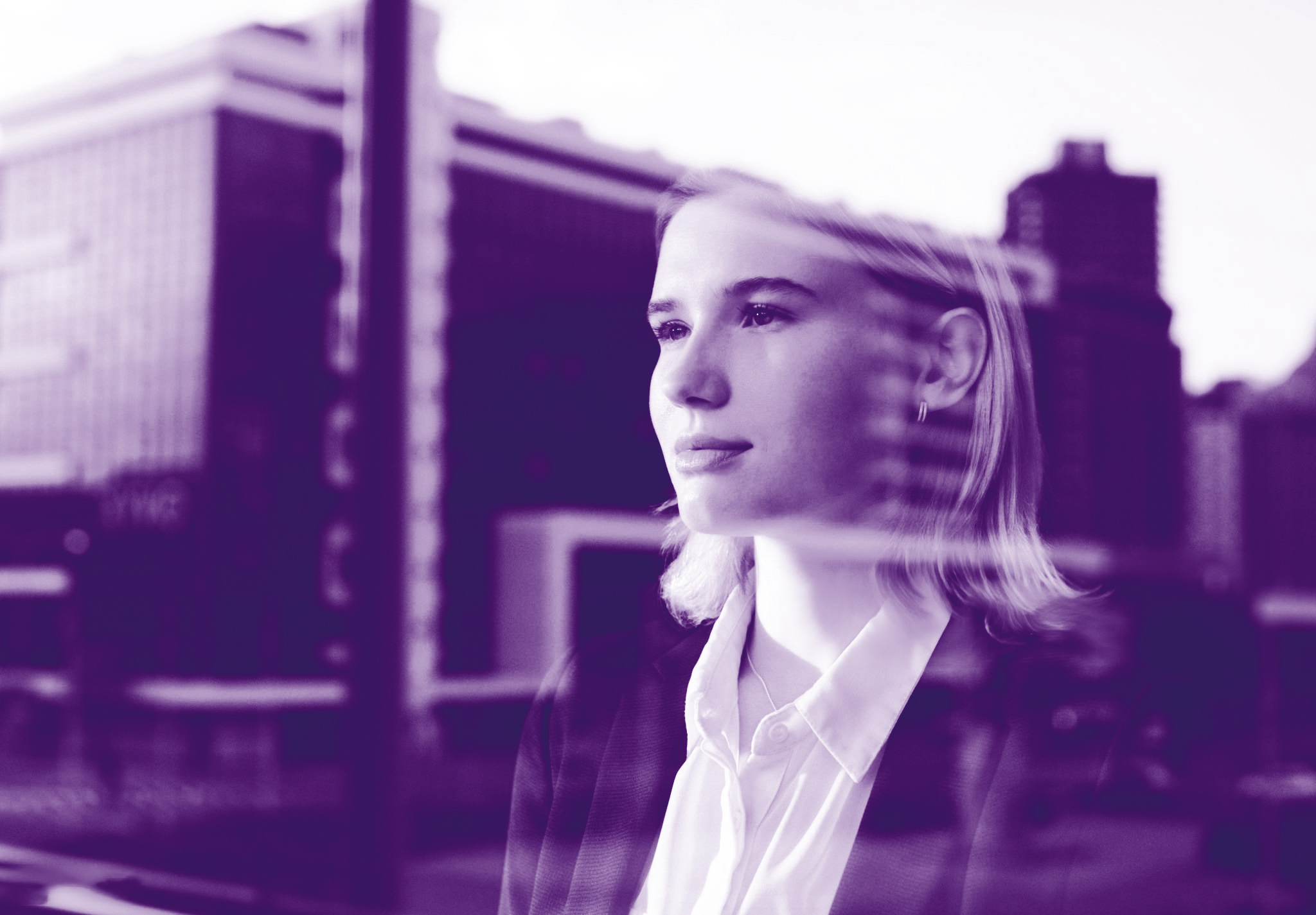 foto con gradiente viola dove si può ammirare una donna bionada che guarda fuori dalla finestra e sullo sfondo si vedono riflessi i palazzi che stanno di fronte