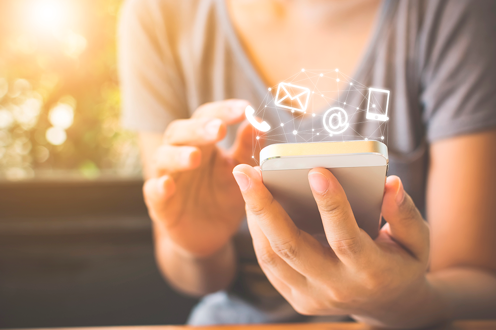 persona che tiene in mano un telefono cellulare e sopra le icone del telefono, busta, @ e cellulare