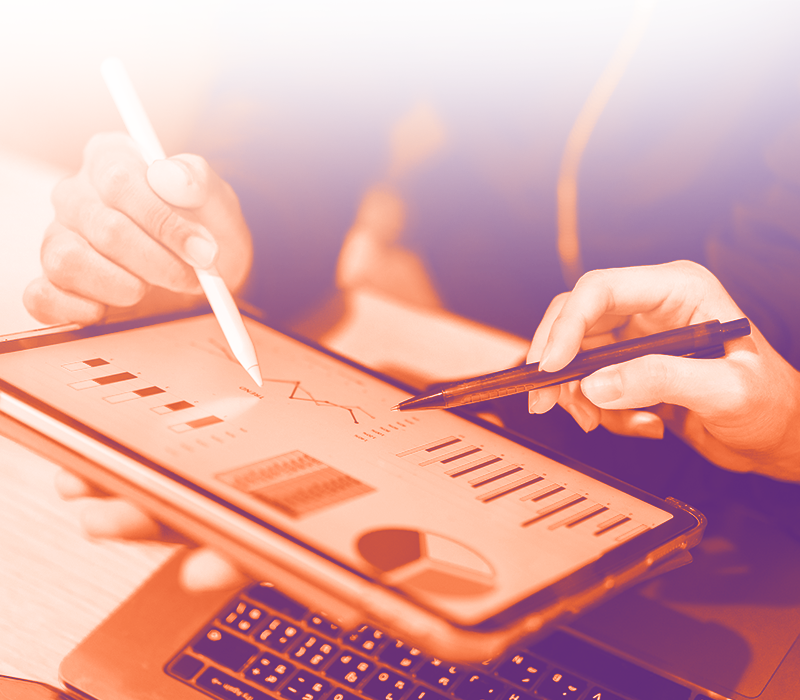 foto con gradiente arancione dove in primo piano c'è un tablet con grafici statistici della bi e delle mani con delle penne che indicano questi grafici