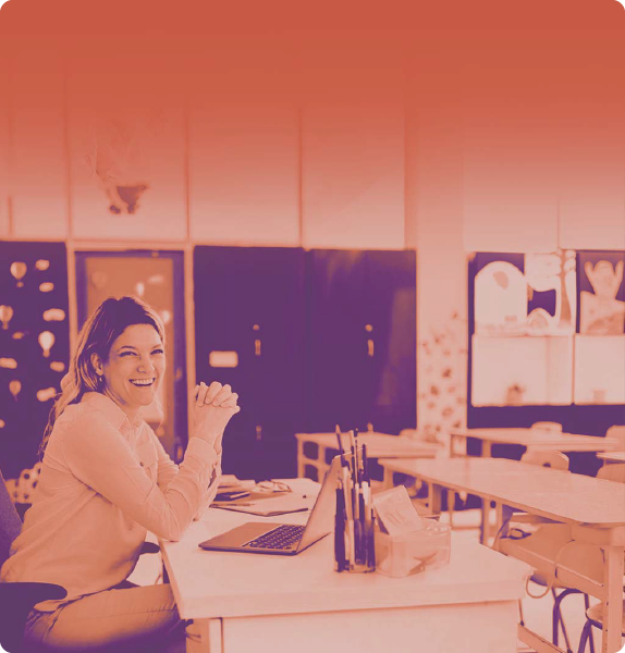 foto con gradiente arancione chiaro che rappresenta un'insegnante seduta sulla cattedra di profilo che sorride e di fronte a lei banchi di scuola senza i bambini seduti