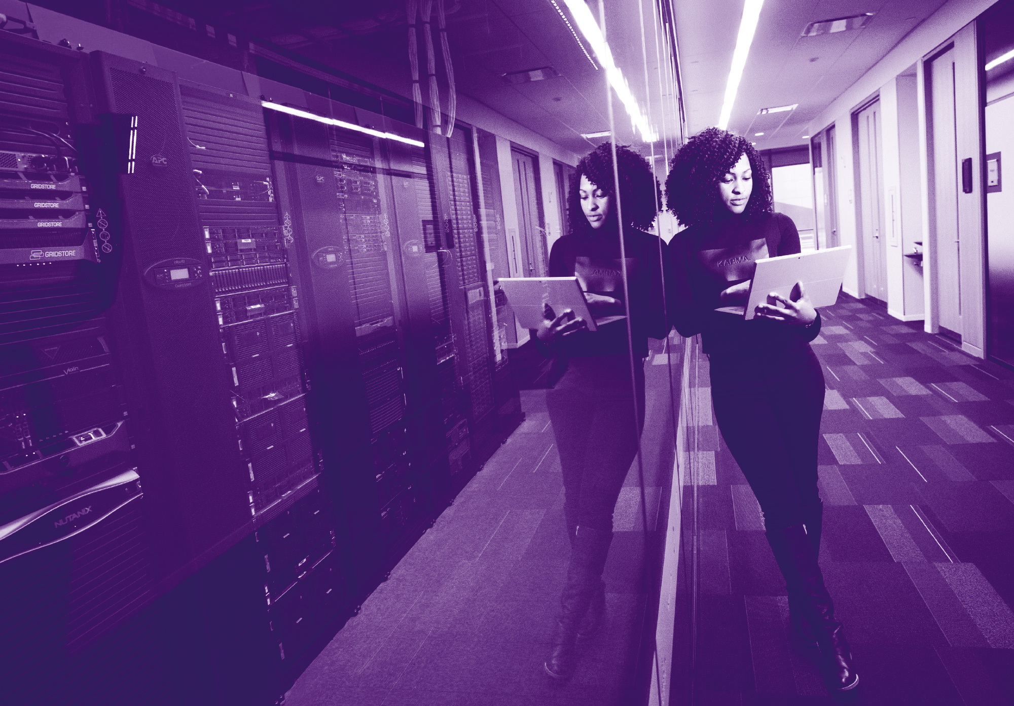 immagine di colore viola che raffigura una donna che tiene in mano un pc all'interno di una stanza server per raffigurare la cyber security