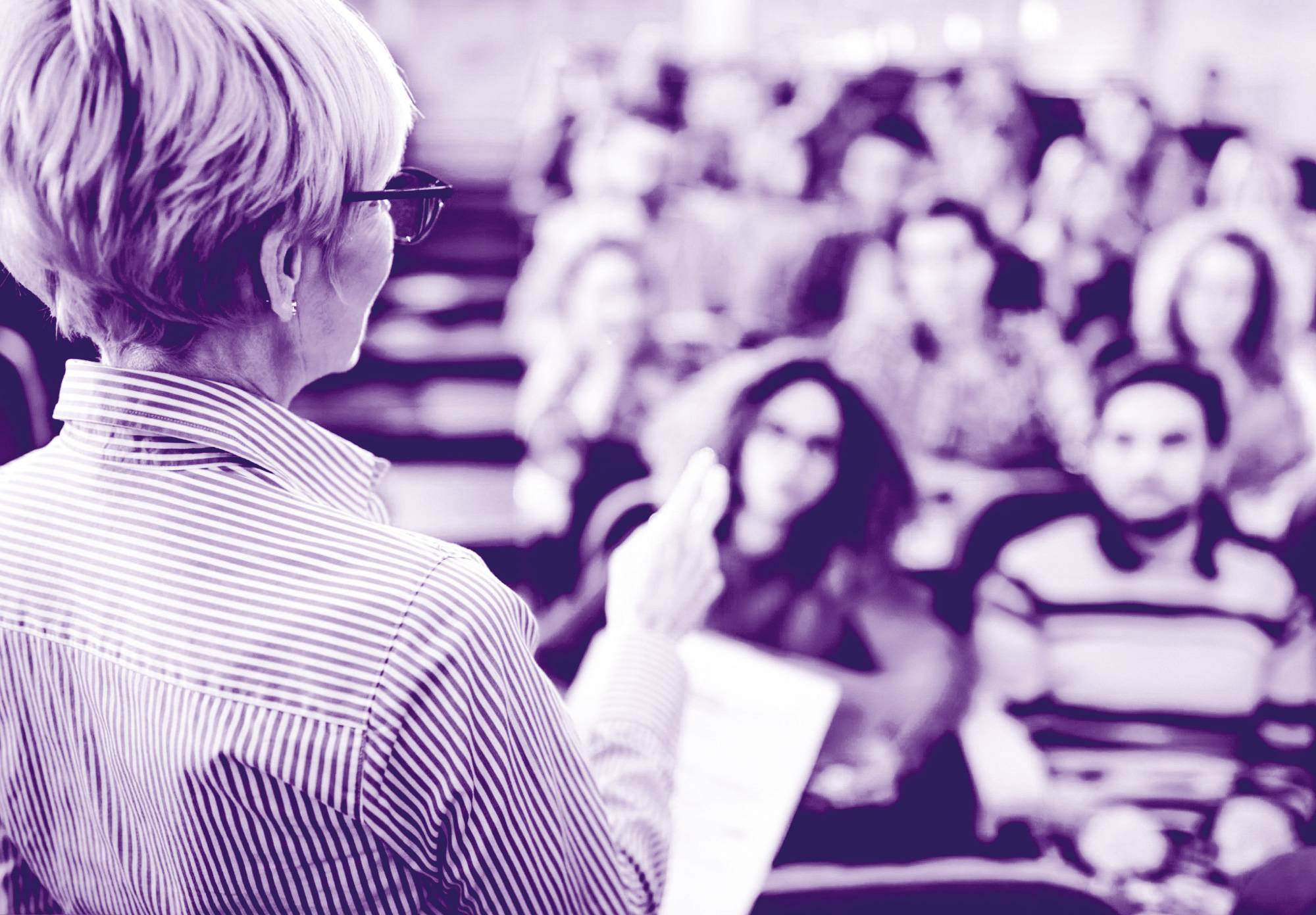 foto con gradiente viola dove si vede in primo piano una insegnante di spalle che sta spiegando ad un pubblico di ragazzi che si vedono sullo sfondo